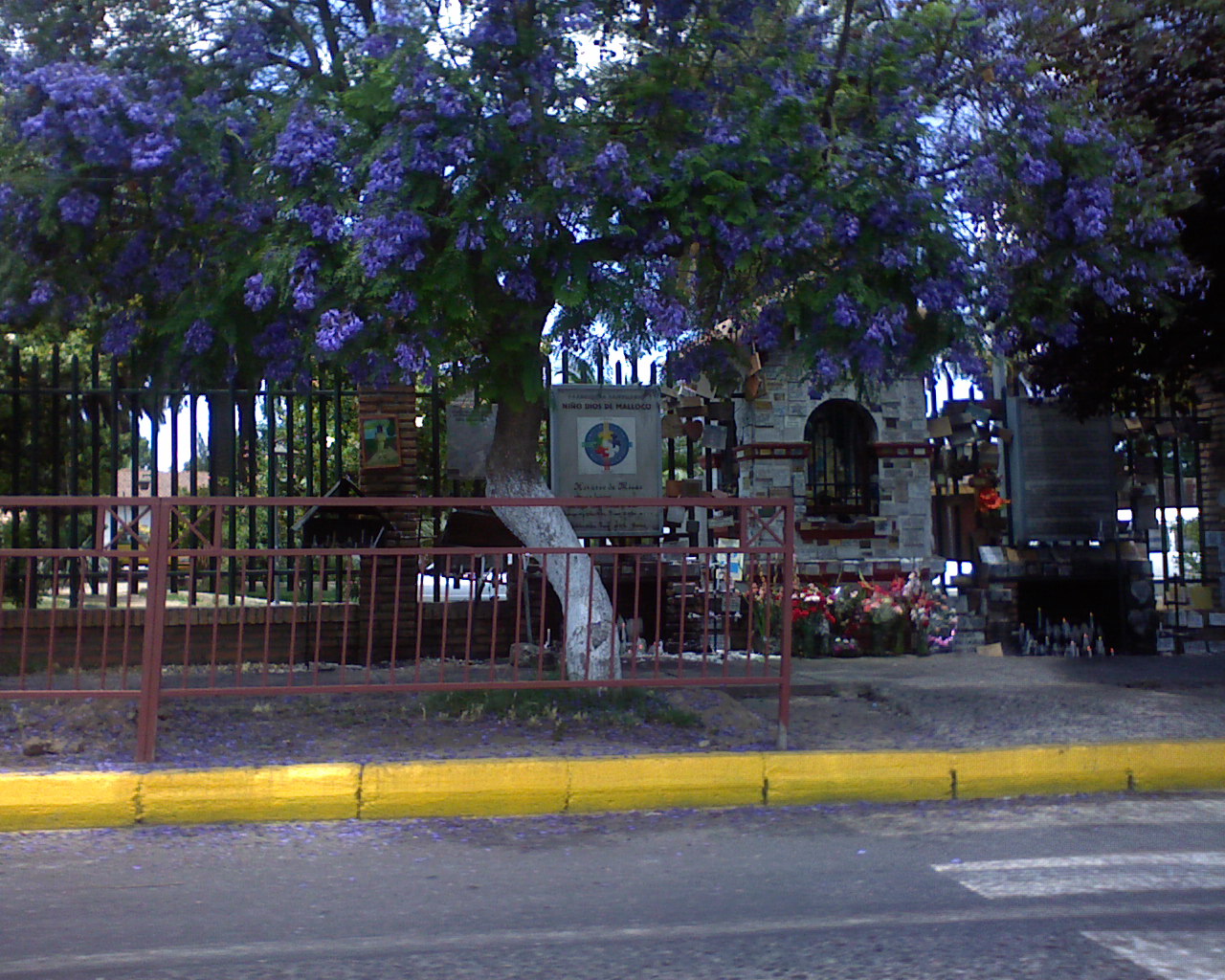 an old building and iron fence with trees and flowers behind it