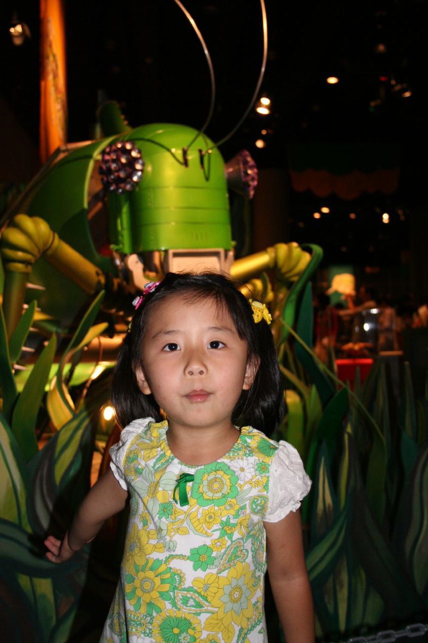 a little girl with a green alien statue behind her