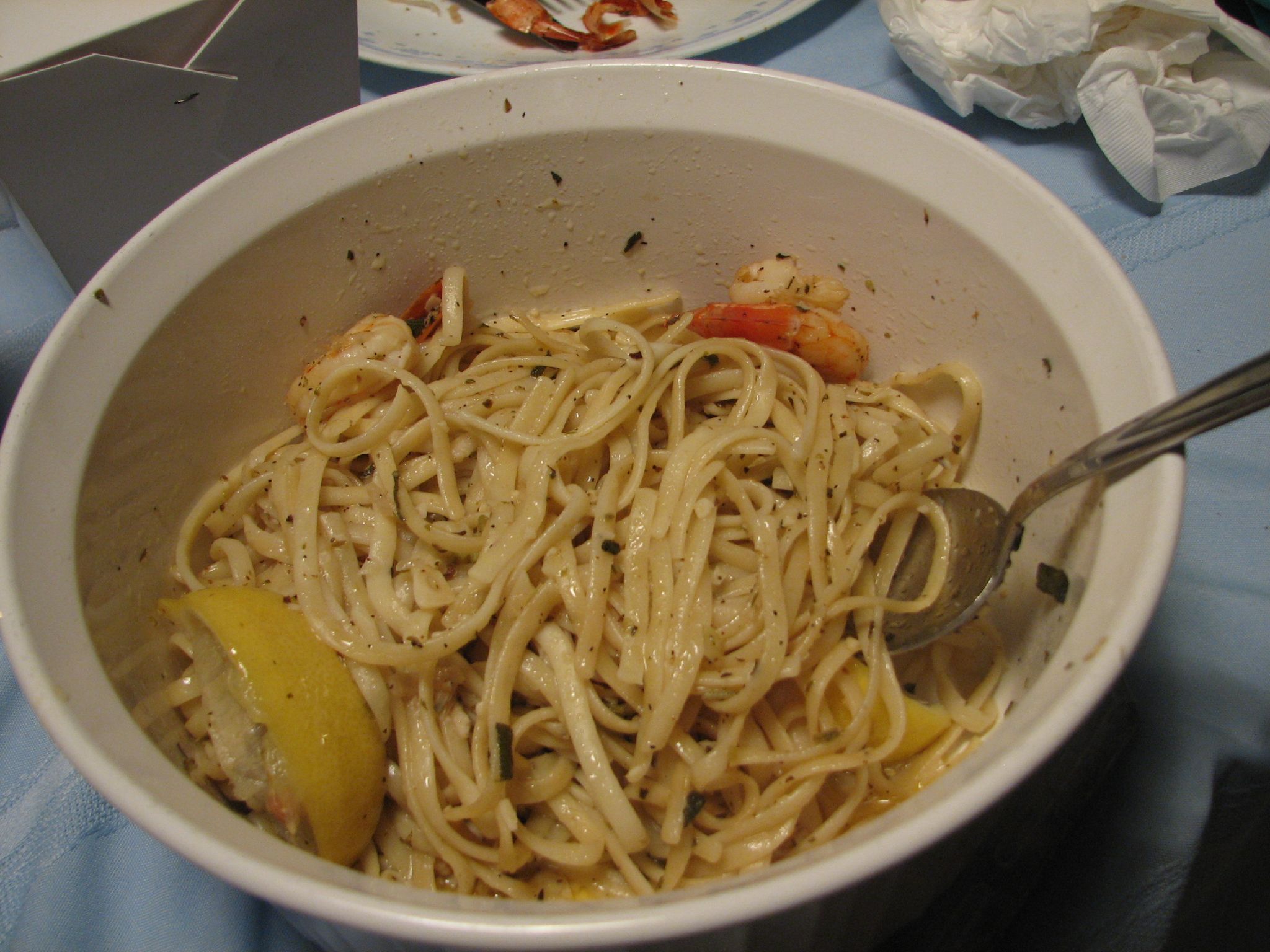 a bowl of shrimp and tomato pasta on a blue tablecloth