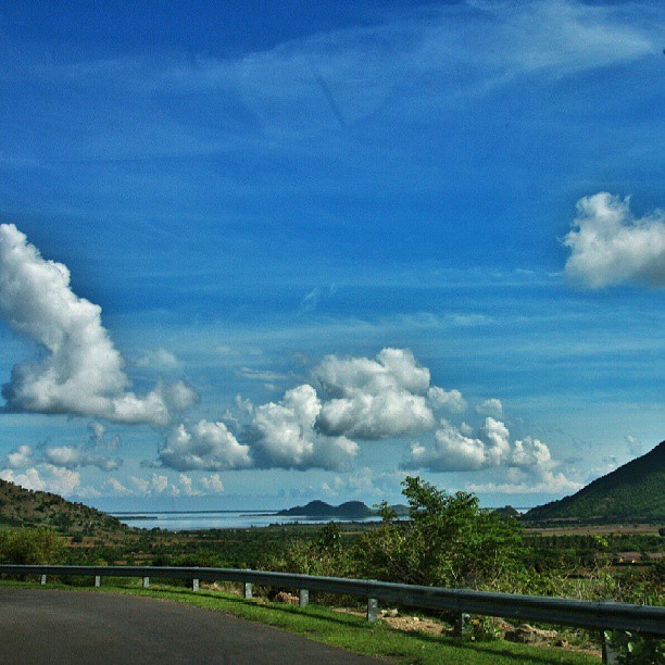 the road curves away from the mountains under a cloudy blue sky
