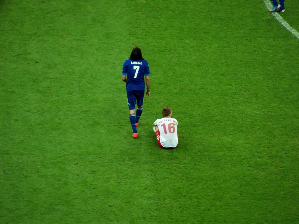 a soccer player is sitting on the ground as he looks at another person who is walking behind him