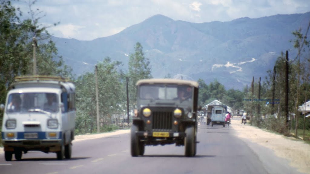 two vehicles drive down a wide road with mountains in the background