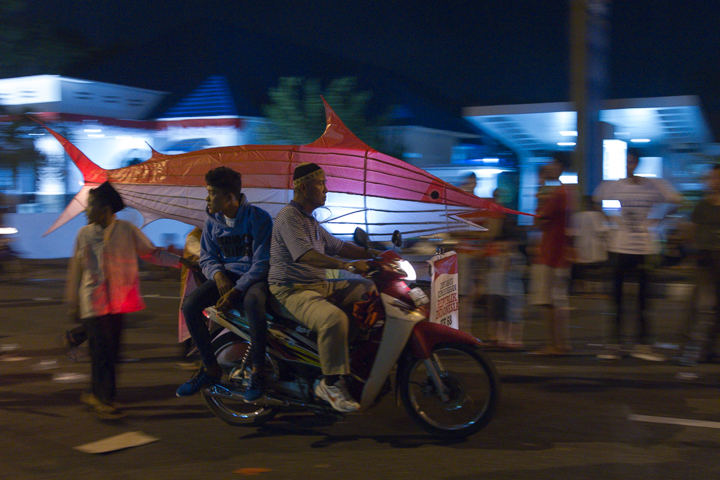 people walking and sitting on a motorcycle with parasols in the background