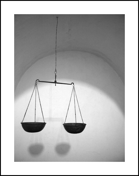 two suspended black balance scales and a shadow on the wall