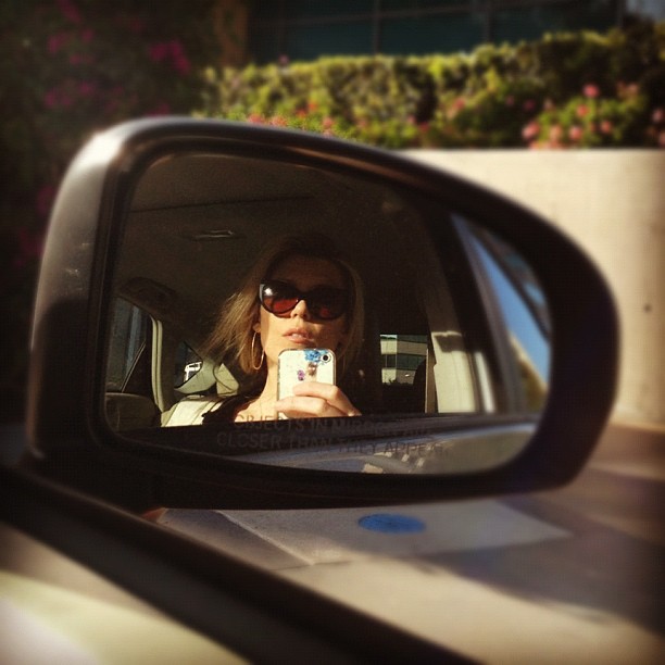 a woman taking a picture from the rear mirror of her car