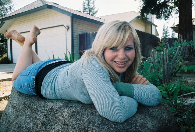 blond woman sitting on a rock in front of house