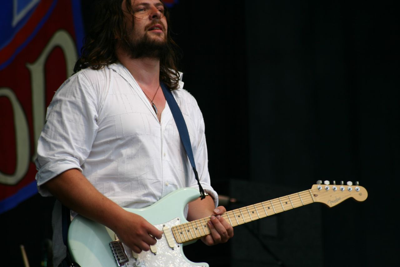 a bearded man with long hair playing a guitar on stage
