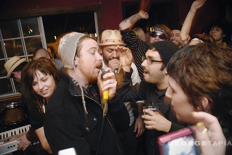 people at a party, with one singing into a microphone and another standing by himself
