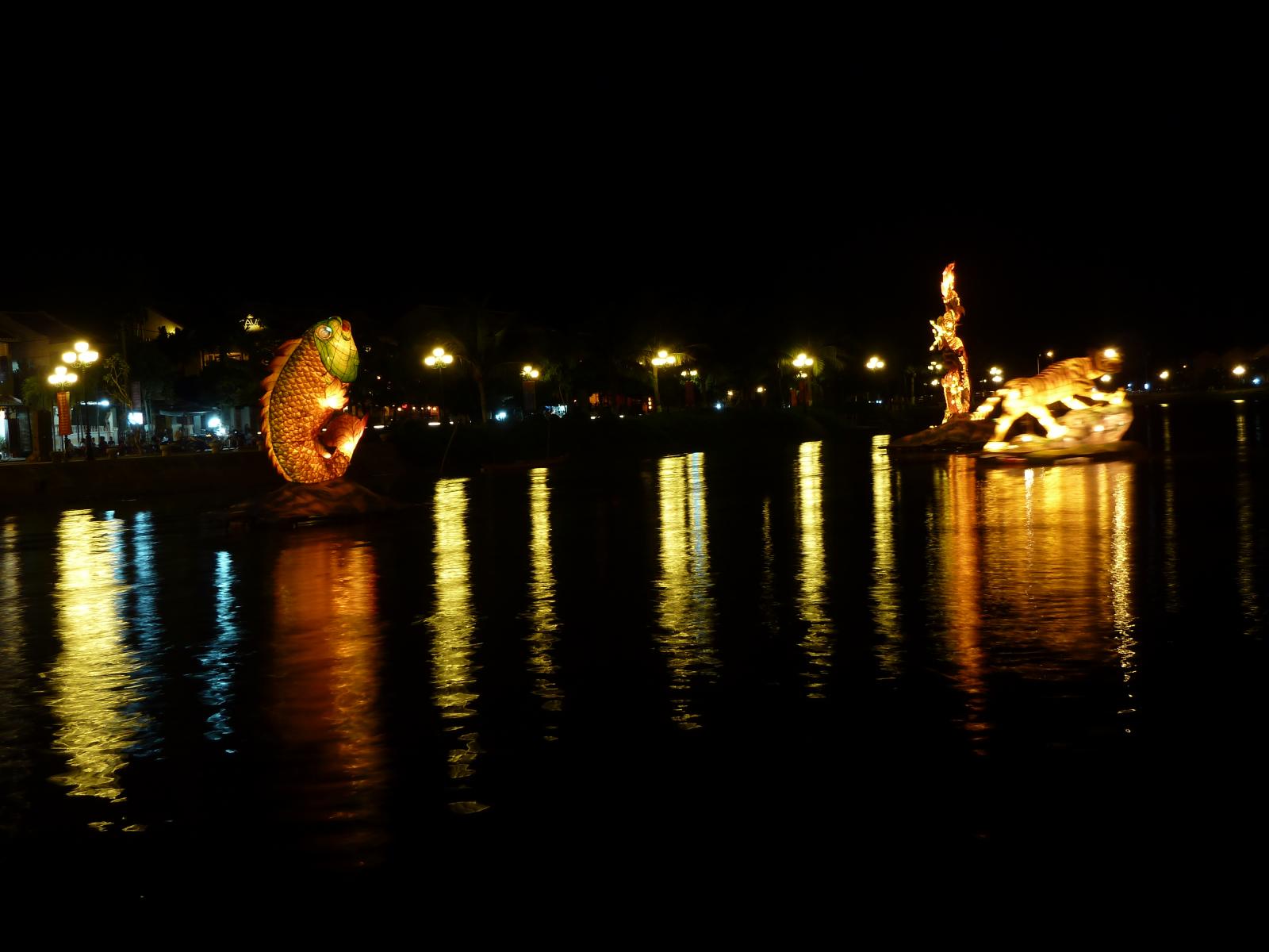 some boats in the water near lights and trees