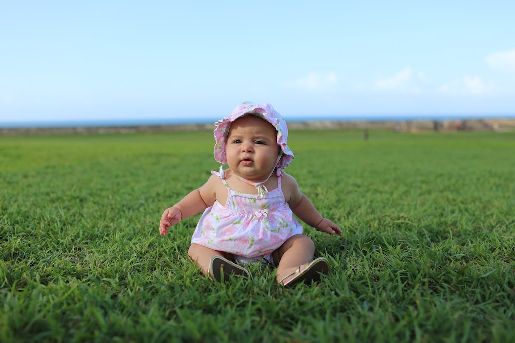 a small baby girl sitting in the middle of a green field