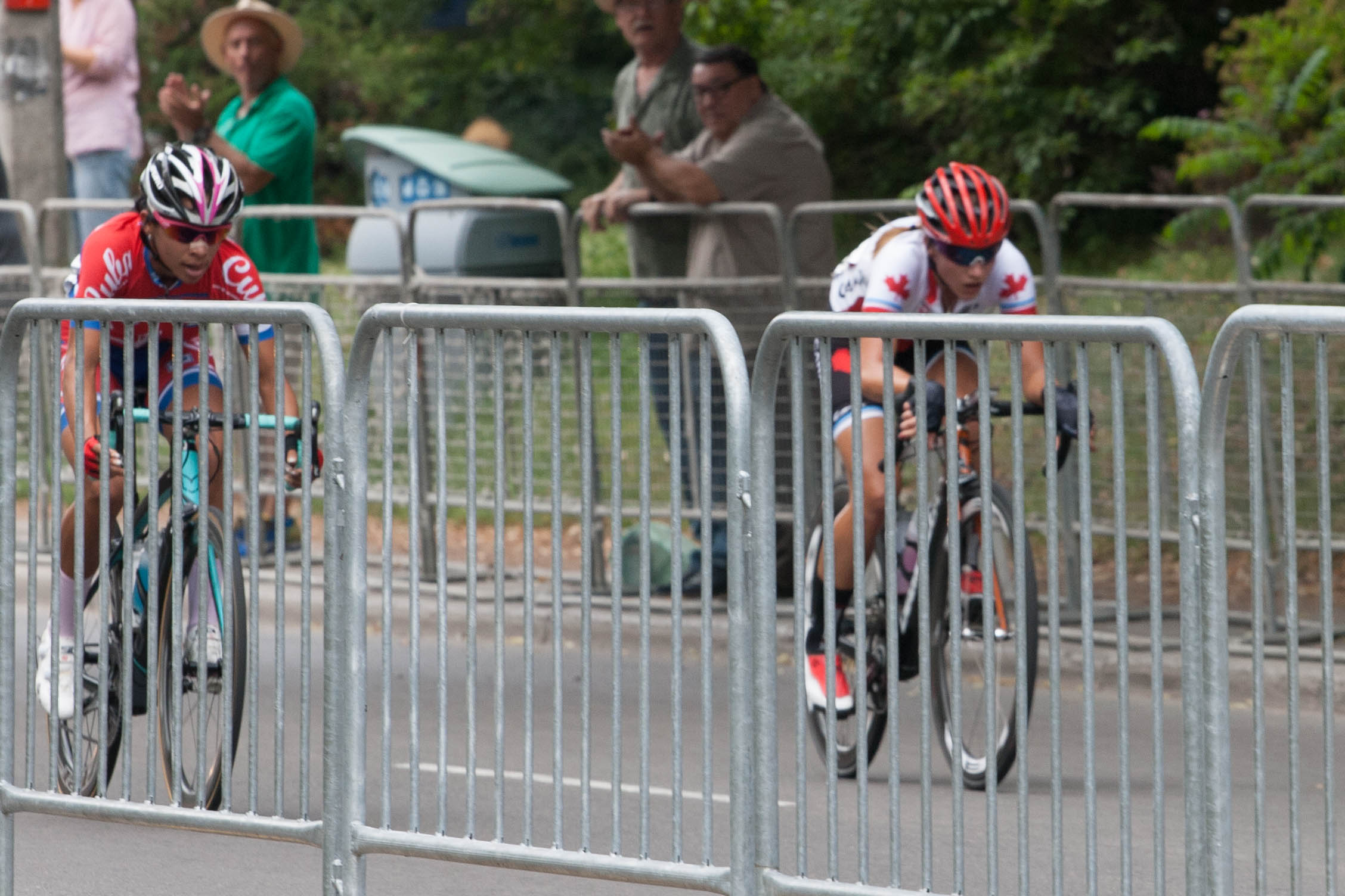 two cyclists in red and white gear riding behind silver barrier posts