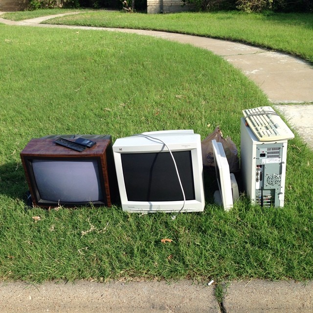 three televisions and microwaves on a lawn in the grass