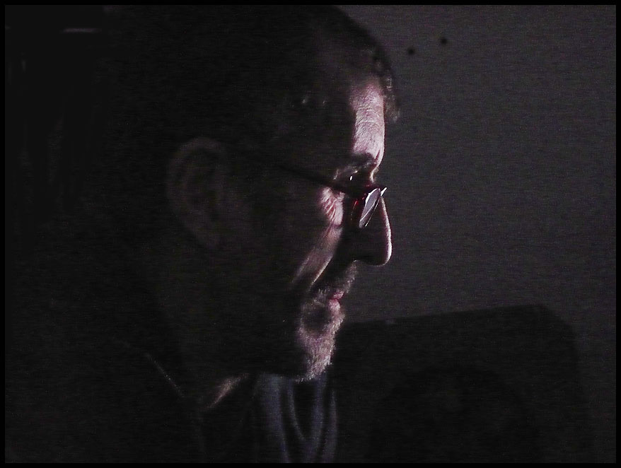 a man in dark with his face down talking on the phone