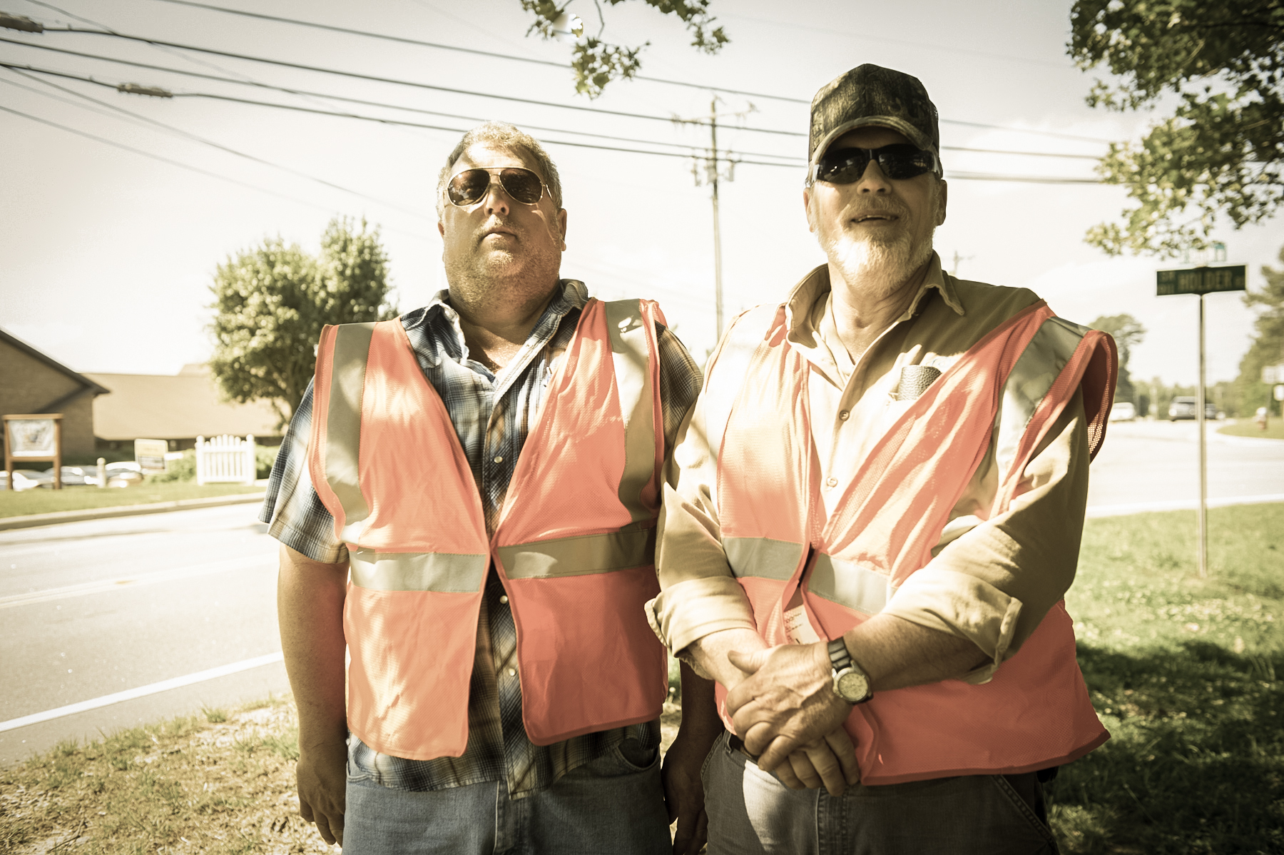 two men in safety vests standing on the side of a road