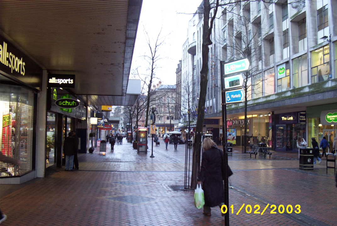 a city street with people on it has shops, stores, and a bench on the sidewalk