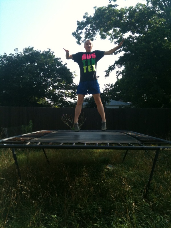 a man is jumping on a black trampoline in the yard