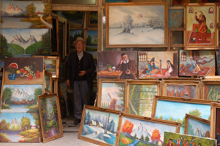 the man is standing near a large collection of framed paintings