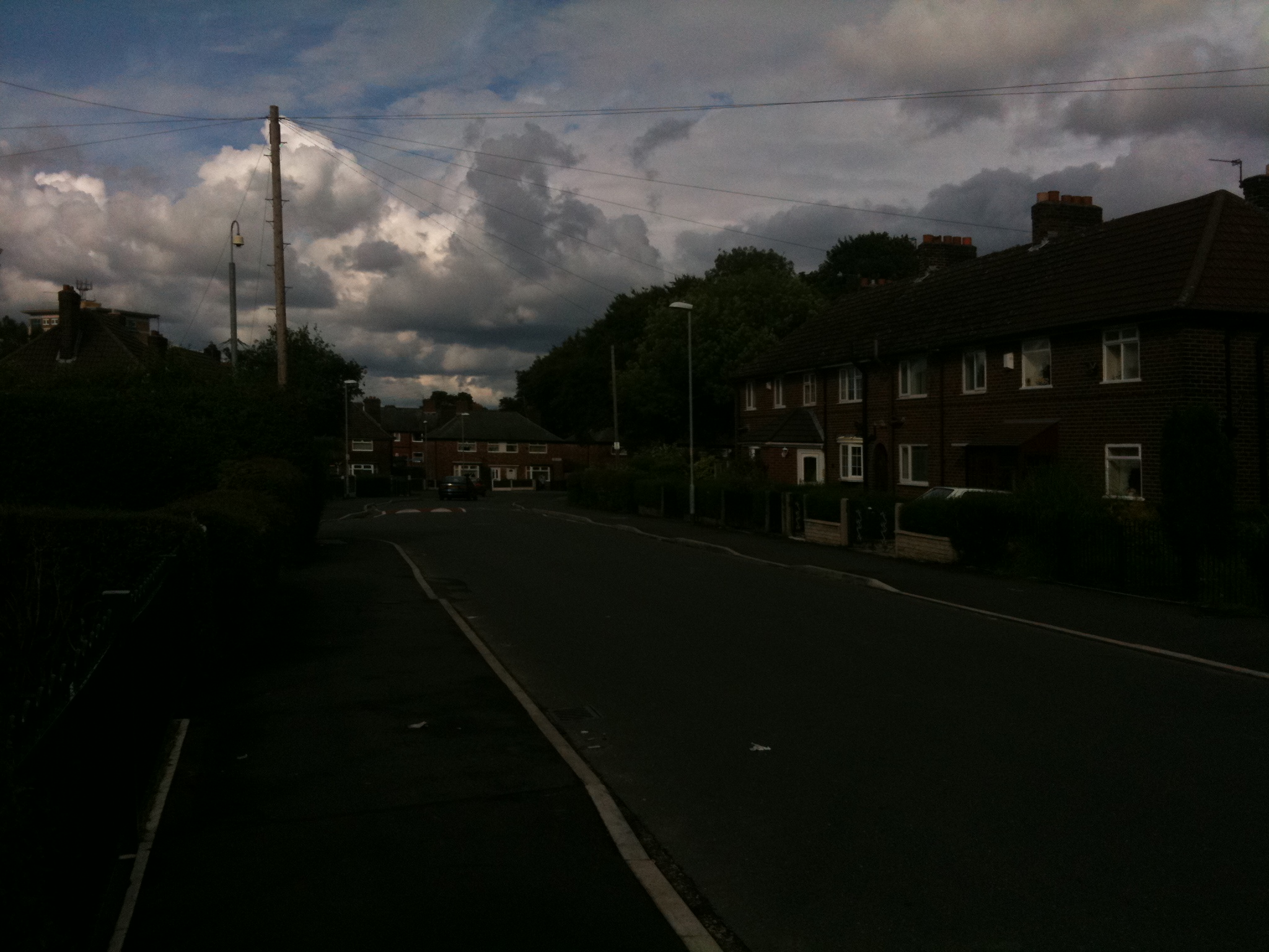 a dark street with a cloudy sky over houses