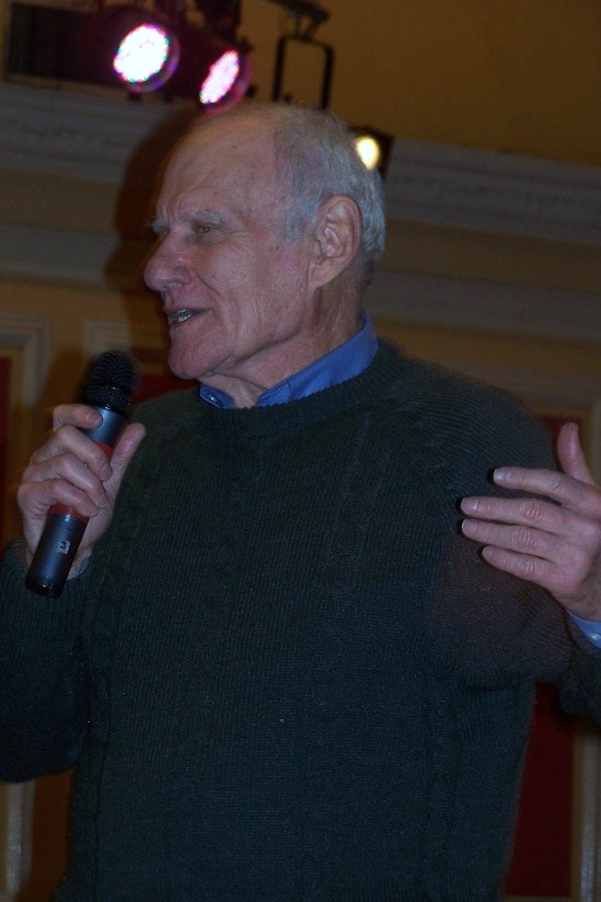 an old man is standing with his hands up while talking into a microphone