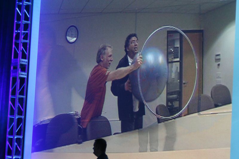 two men are on stage talking with one man holding a large disc