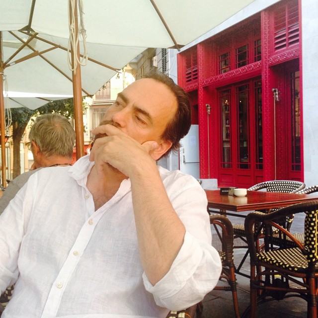 a man sitting at an outdoor cafe drinking coffee