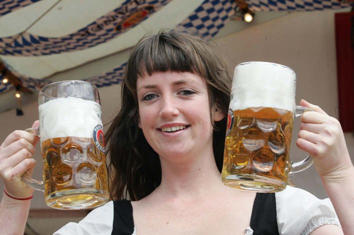a woman holding two glasses of beer with one person smiling
