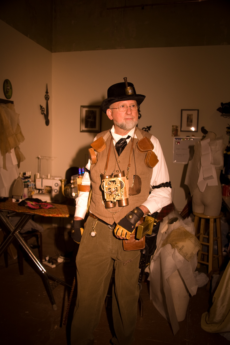 a man dressed in steampunk clothes is standing in a room full of old clothing