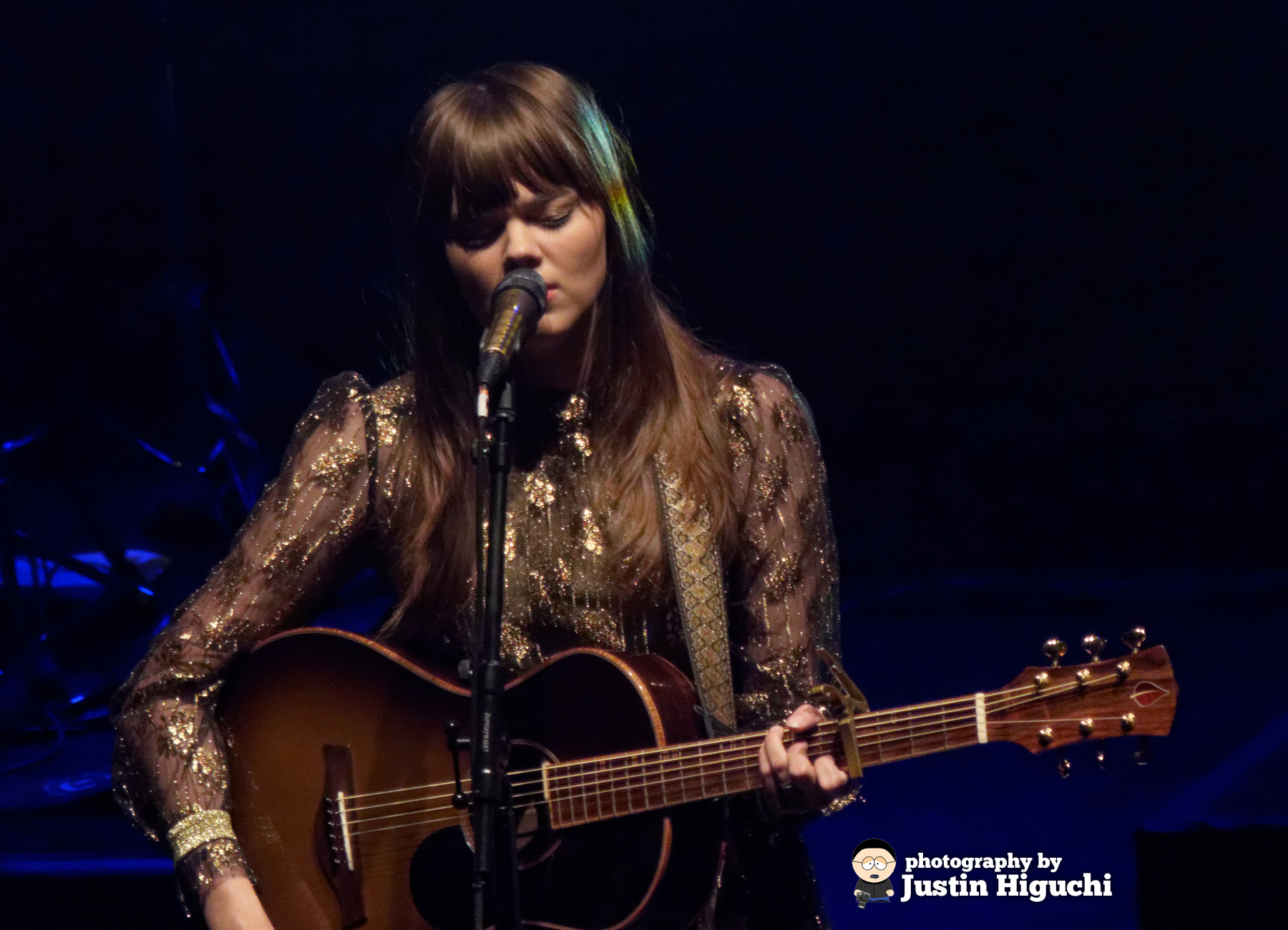 a young woman sings into the microphone while holding an acoustic guitar