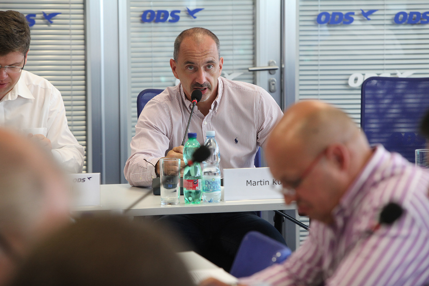 three men sitting at a table and one is speaking