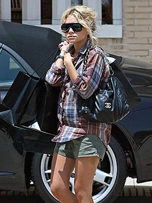a woman in a plaid shirt is walking near a car and talking on the phone