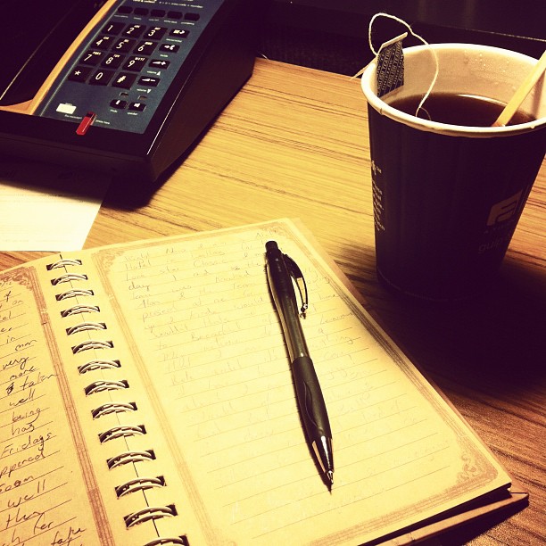 an open book on a wooden desk next to a cup and a keyboard