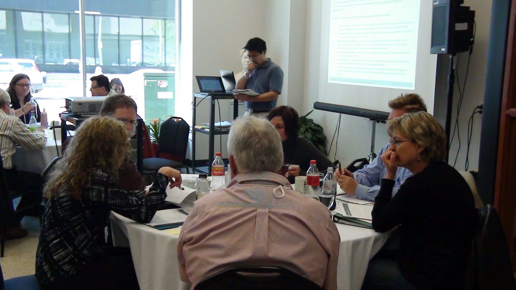 a group of people sitting at tables in front of a presentation