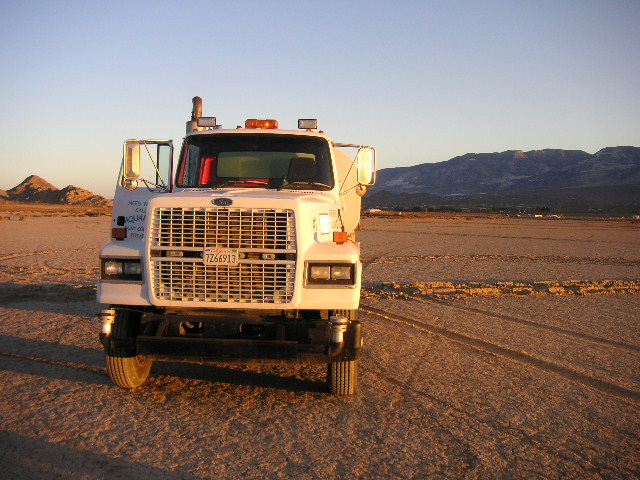 a truck driving in a dirt field with hills and mountains