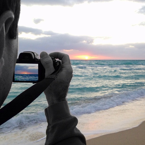 the man is taking a picture of the sunset over the ocean