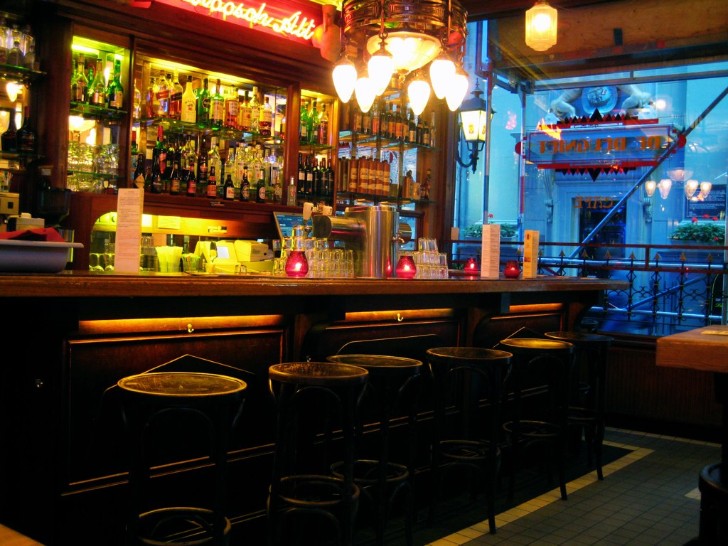 several tables with stools under lit up lights and a bar