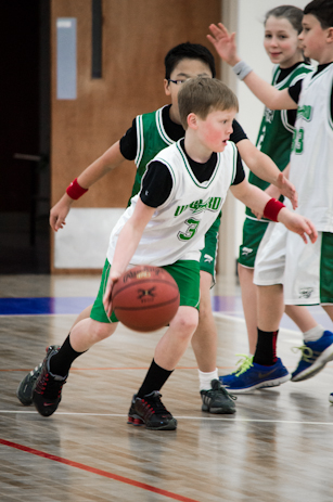 young children in green and white uniforms playing basketball