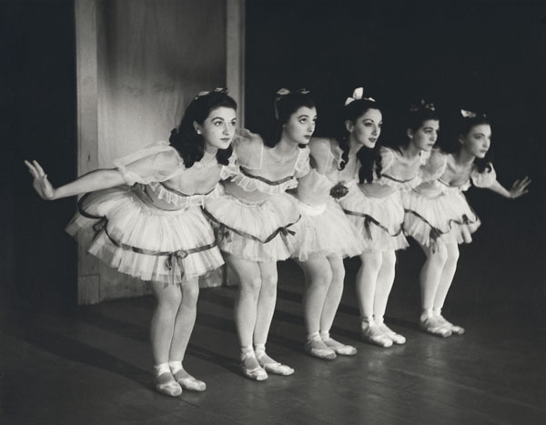 several young ballerinas performing on stage with one woman holding soing