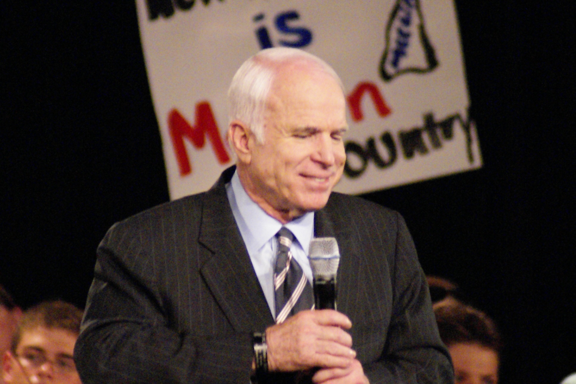 a man in a suit holds a microphone as others sit