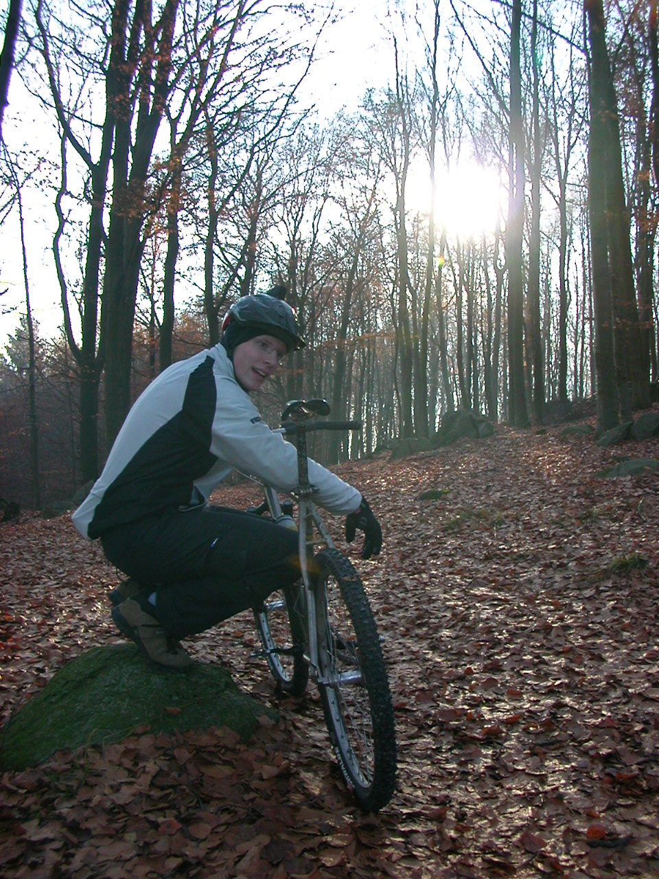 a man kneeling on a fallen tree while holding a bicycle