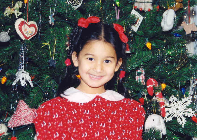 a girl in a red sweater with a knitted shirt on is standing in front of a christmas tree