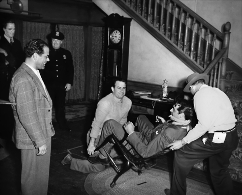 two men in suits standing by a man laying on the floor