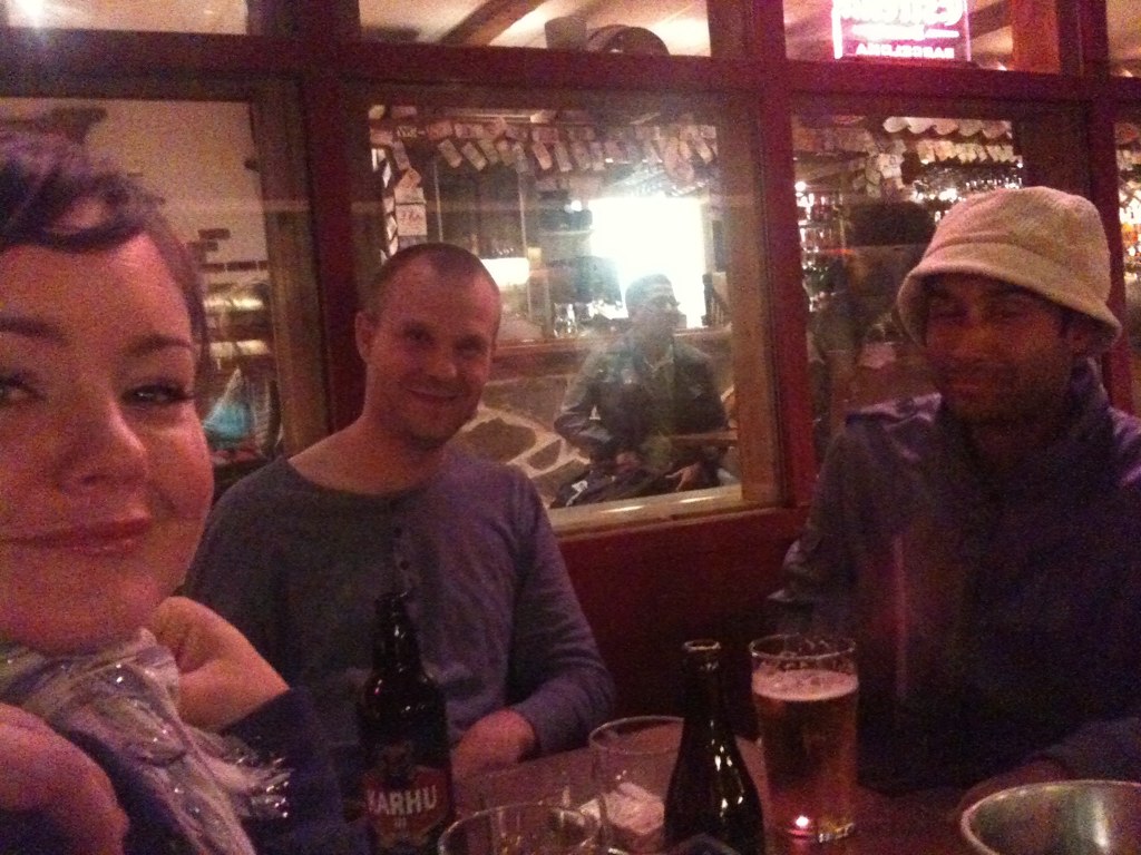 two men and a woman sitting at a table with beer glasses