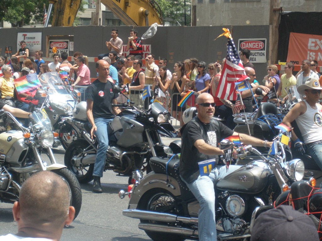 several motorcyclists in the road are carrying american flags