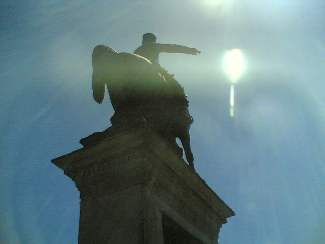 a statue atop a tall building with sun rays streaming through