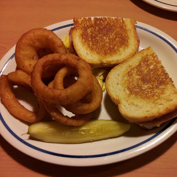 some onion rings and an english muffin are on a plate with pickles