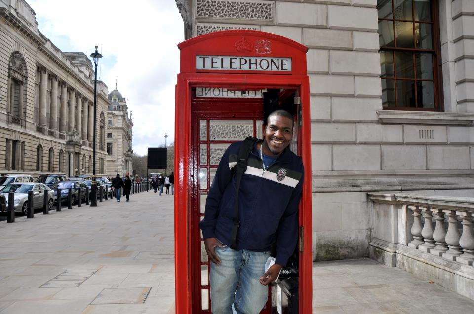 a smiling man stands in the door of a red telephone booth