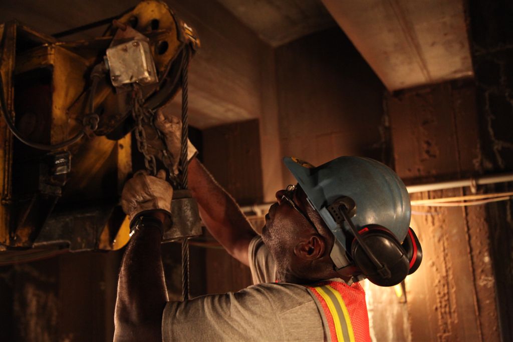 a man in safety gear holding on to a beam while wearing a hard hat