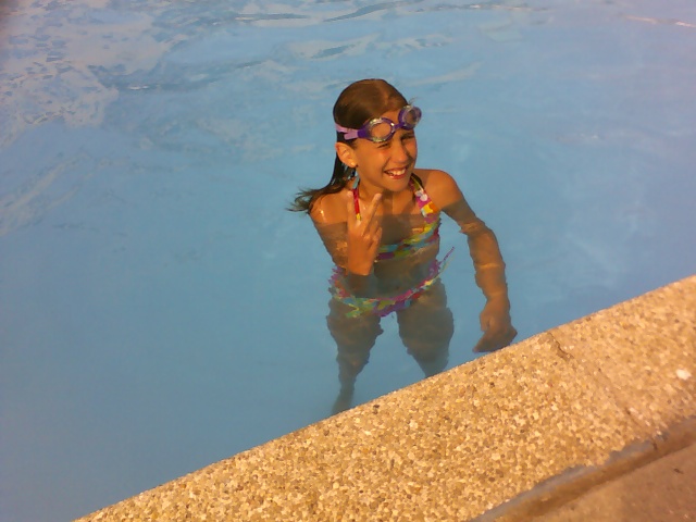 a girl in a pool with sun glasses on posing for a picture