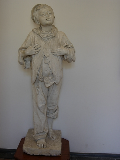 the statue in the corner of the room shows a boy standing with his arms crossed