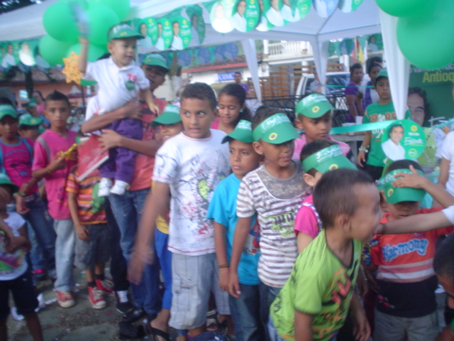 a group of children with hats standing under green balloons